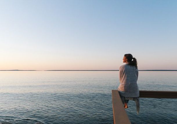 Finanzielle Freiheit erreichen - Frau sitzt am Wasser und denkt nach