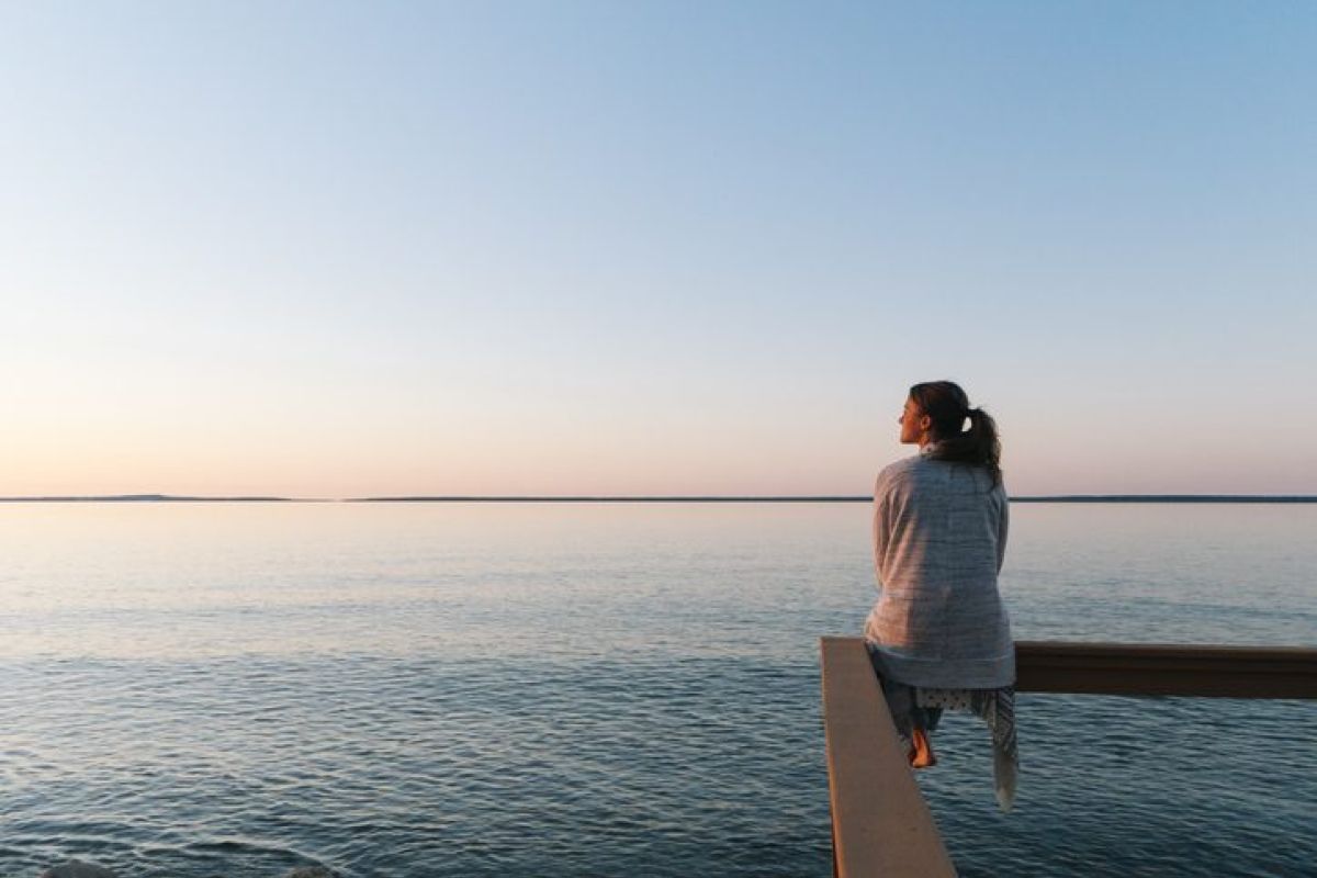 Finanzielle Freiheit erreichen - Frau sitzt am Wasser und denkt nach