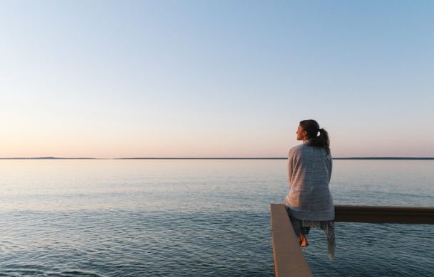 Finanzielle Freiheit erreichen - Frau sitzt am Wasser und denkt nach