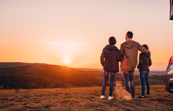 Familie mit Hund umarmt am Hügel und Blick auf den Sonnenuntergang