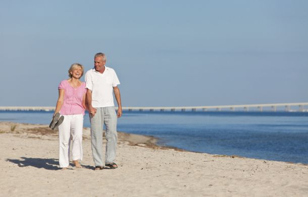 Ein glückliches Seniorenpaar geht Hand in Hand am Strand entlang