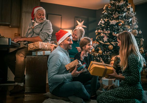 Eine fröhliche Familie sitzt vor einem festlich geschmückten Weihnachtsbaum und packt strahlend Geschenke aus.
