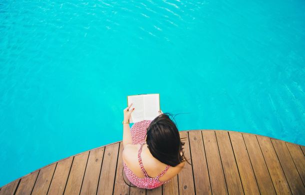 Frau am Pool beim Buch lesen