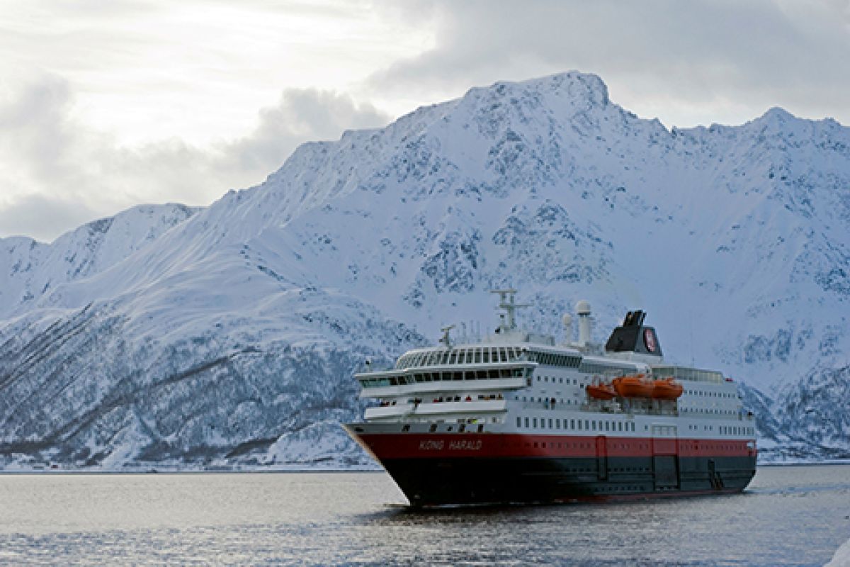 Ein Postschiff fährt auf dem Wasser vor der malerischen Kulisse Norwegens während einer Kreuzfahrt.
