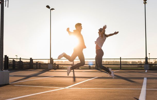Unbekümmertes junges Paar, das bei Sonnenuntergang auf einem Parkdeck springt