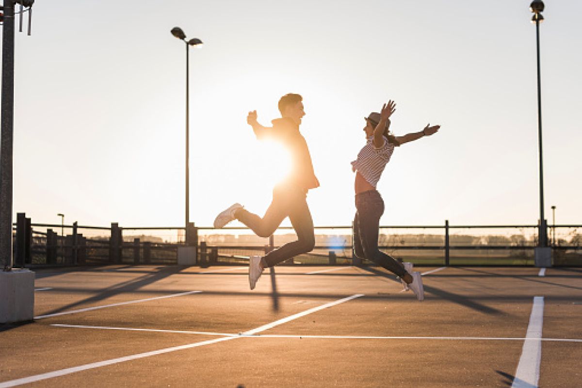 Unbekümmertes junges Paar, das bei Sonnenuntergang auf einem Parkdeck springt