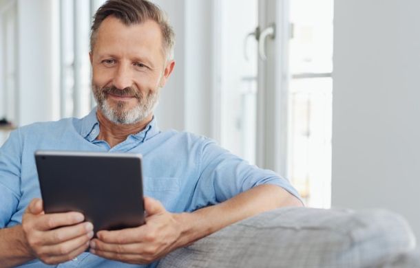 Attraktiver Mann entspannt auf einem Sofa mit einem Tablet-PC