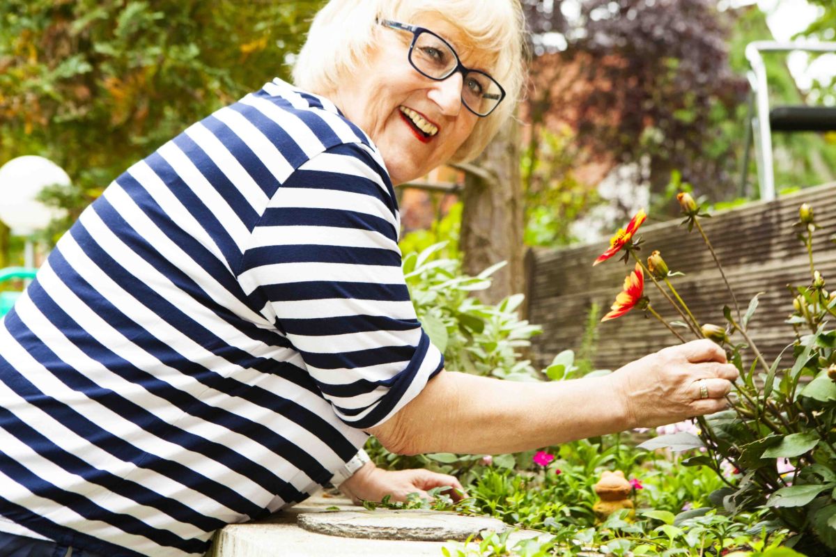 Eine ältere Frau im Garten, die sich um ihre Blumen kümmert.