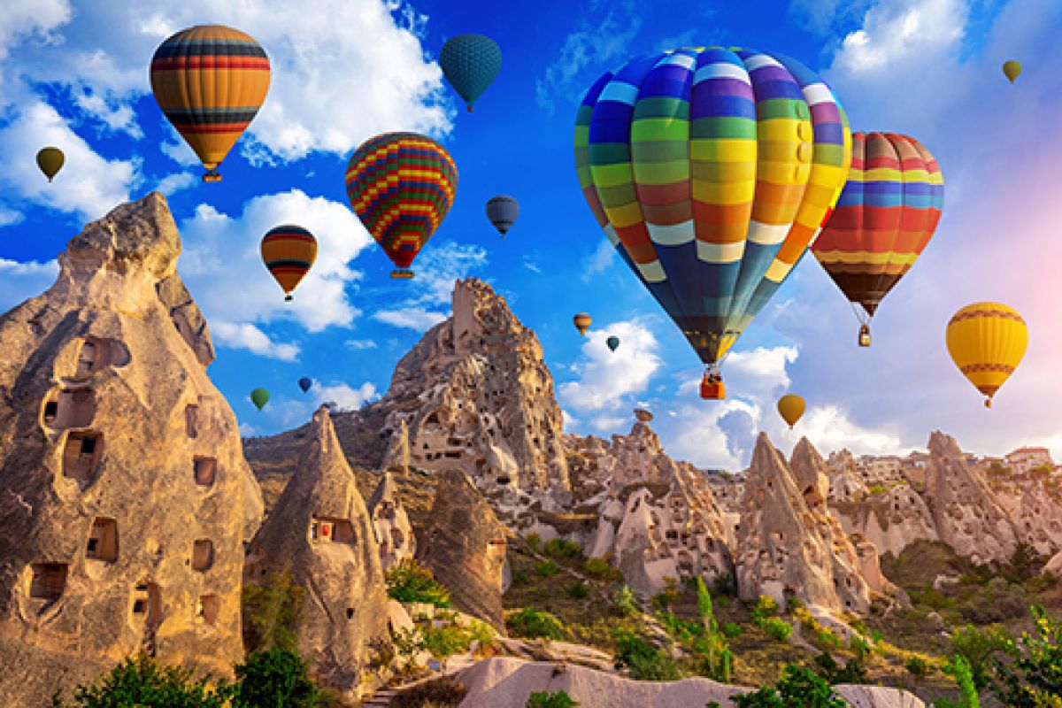 Mehrere bunte Heißluftballons steigen in den Himmel, umgeben von weißen Wolken und strahlendem Sonnenschein.