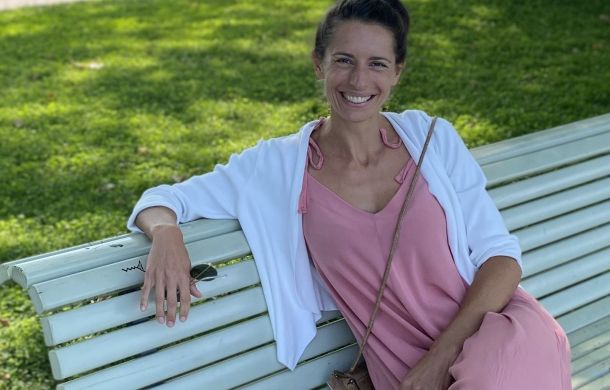 Frau in einem rosa Kleid, die auf einer Bank sitzt und lächelt.
