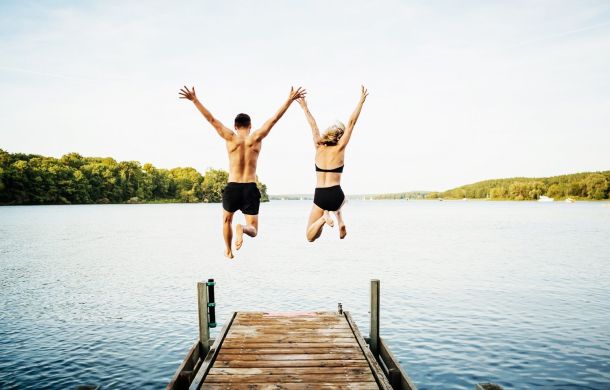 Zwei Freunde springen gemeinsam vom Steg am See