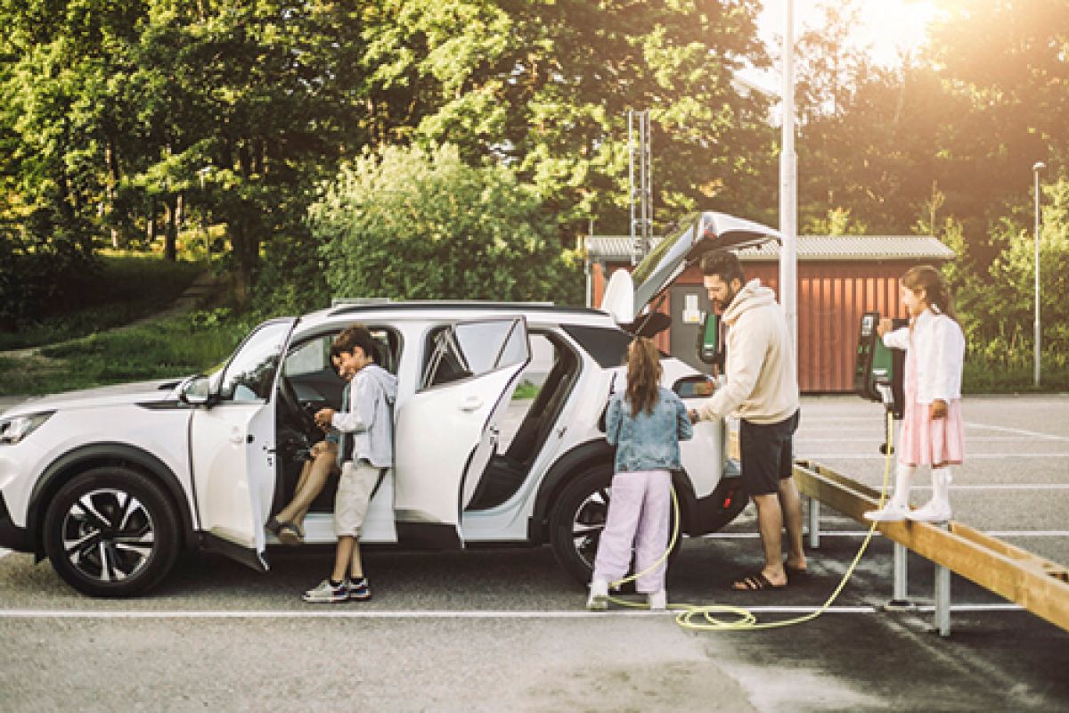 Familie auf einem Ausflug, parkend auf einem Parkplatz und beim Aufladen ihres E-Autos an einer Ladestation.
