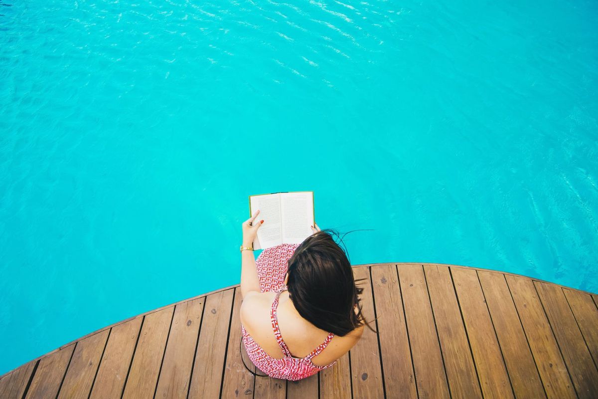 Frau am Pool beim Buch lesen