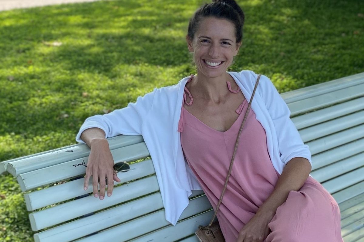 Frau in einem rosa Kleid, die auf einer Bank sitzt und lächelt.