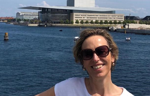Frau lächelt am Wasser, mit einer Küste im Hintergrund.