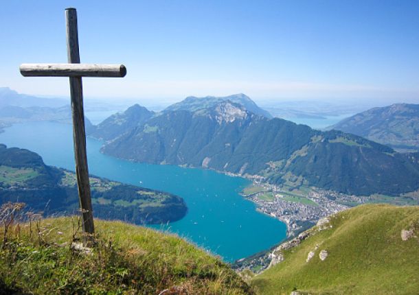 Landschaft auf einem Hügel mit Blick auf einen See, auf dem Hügel steht ein Kreuz.