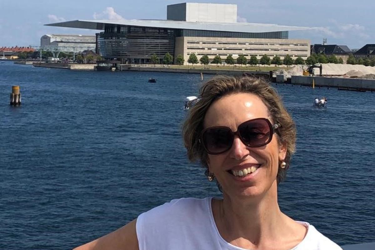 Frau lächelt am Wasser, mit einer Küste im Hintergrund.