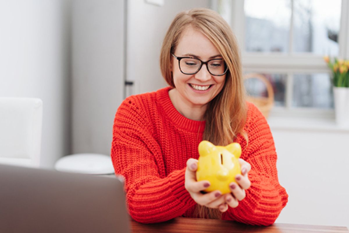 Eine blonde Frau mit einem Sparschwein in der Hand.