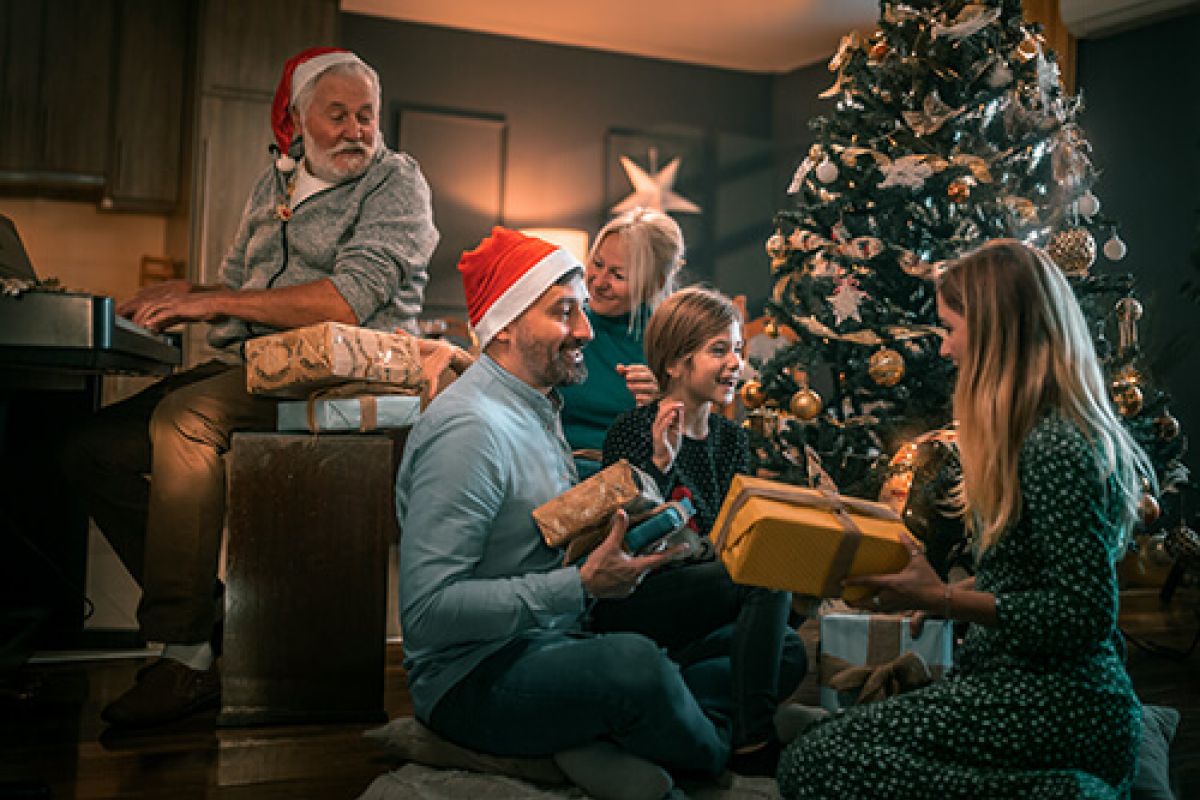 Eine fröhliche Familie sitzt vor einem festlich geschmückten Weihnachtsbaum und packt strahlend Geschenke aus.