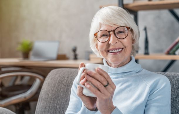 Eine ältere Frau sitzt auf der Couch mit einer Tasse in der Hand und ist eine SKL-Gewinnerin.