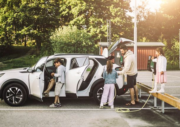 Familie auf einem Ausflug, parkend auf einem Parkplatz und beim Aufladen ihres E-Autos an einer Ladestation.