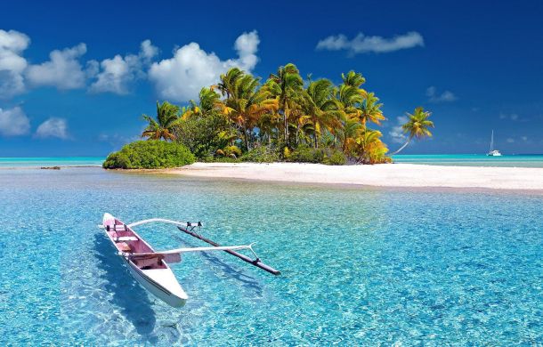 Boot auf dem himmelblauen Wasser, vor einer Insel mit Palmen.