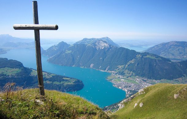 Landschaft auf einem Hügel mit Blick auf einen See, auf dem Hügel steht ein Kreuz.