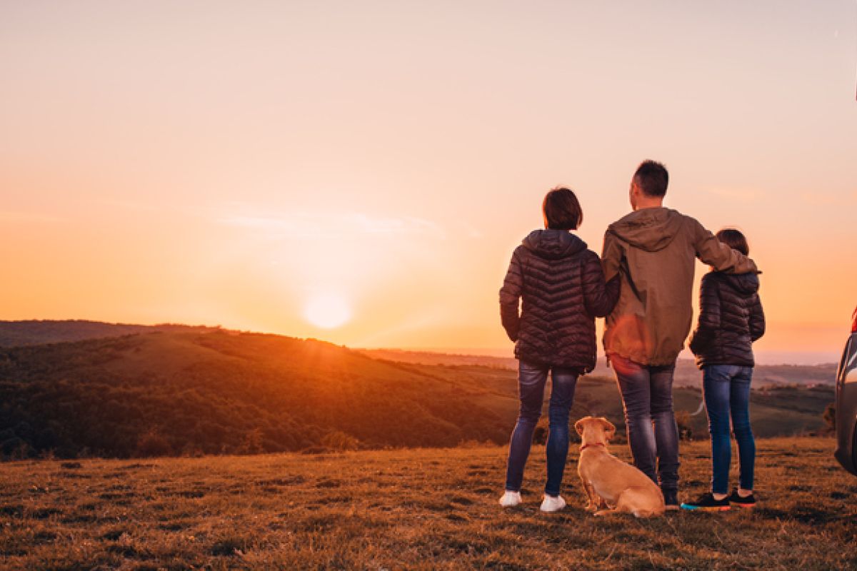 Familie mit Hund umarmt am Hügel und Blick auf den Sonnenuntergang