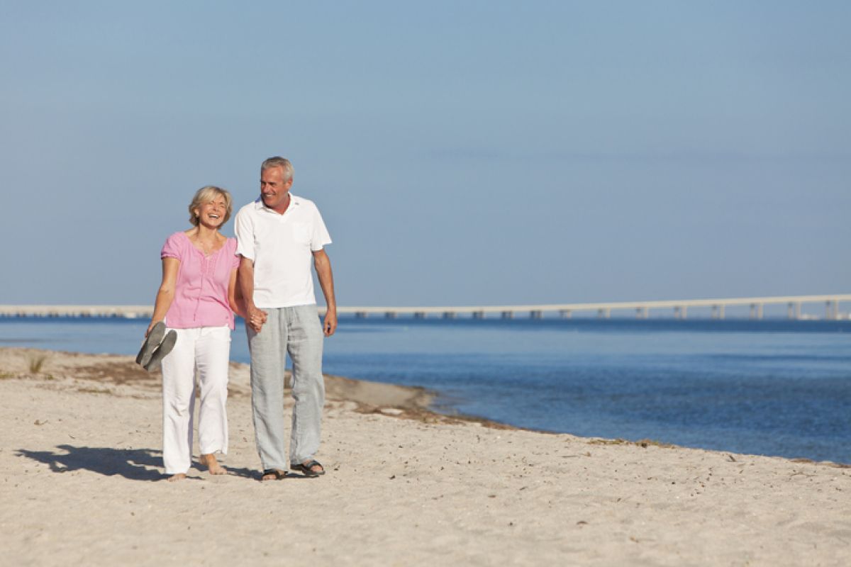 Ein glückliches Seniorenpaar geht Hand in Hand am Strand entlang