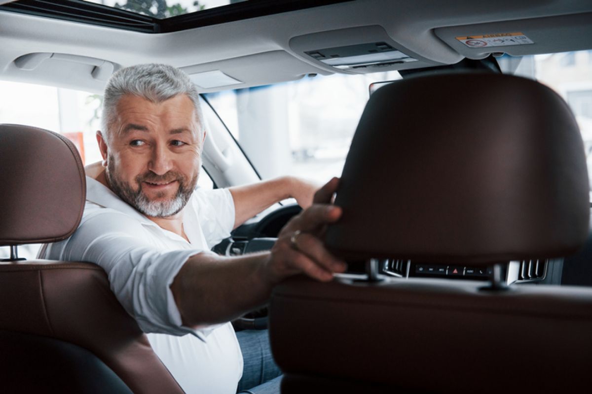 Ein älterer Mann fährt rückwärts mit einem Auto.