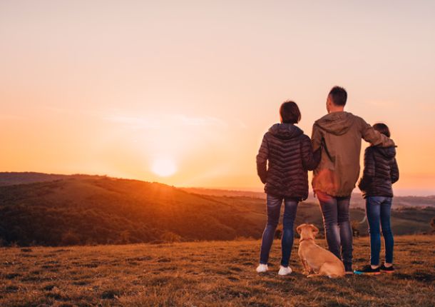 Familie mit Hund umarmt am Hügel und Blick auf den Sonnenuntergang