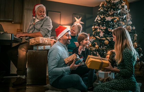 Eine fröhliche Familie sitzt vor einem festlich geschmückten Weihnachtsbaum und packt strahlend Geschenke aus.