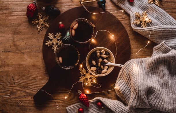 Auf einem Tisch stehen Glühwein, eine Schüssel mit Nüssen und Rosinen sowie eine kleine weihnachtliche Lichterkette.