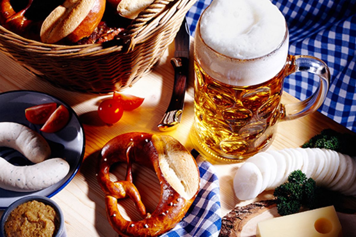 Tisch gedeckt mit einem Maß Bier, einer Brezel und Weißwürsteln.