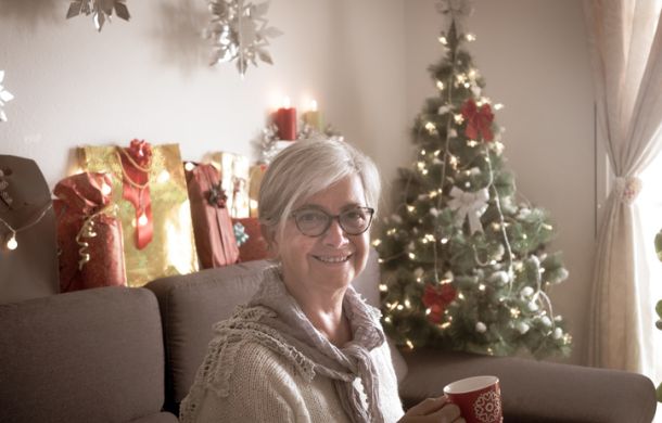 Glückliche Gloeckle Gewinnerin sitzt mit einer Tasse in der Hand auf der Couch, während im Hintergrund ein Weihnachtsbaum steht.