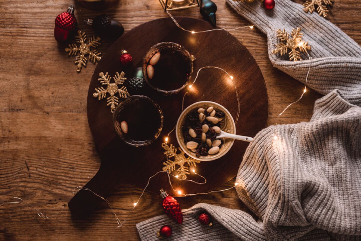 Auf einem Tisch stehen Glühwein, eine Schüssel mit Nüssen und Rosinen sowie eine kleine weihnachtliche Lichterkette.